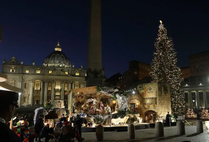 Nativity scene and large Christmas tree in St. Peter's Square at the Vatican, Rome, at night with St. Peter's Basilica illuminated in the background