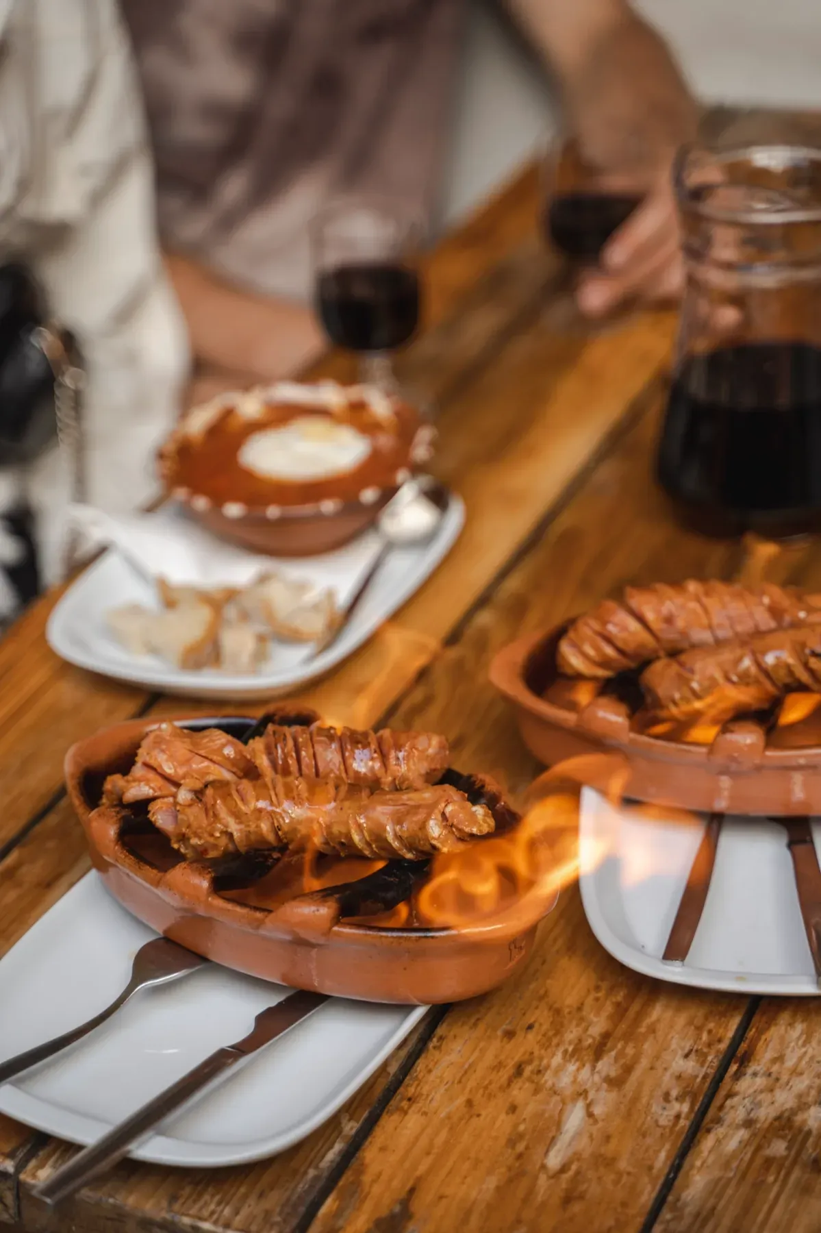 Close-up of traditional Portuguese chouriço sausage flambéed on a rustic wooden table, with red wine and local dishes, during a Lisbon food tour.