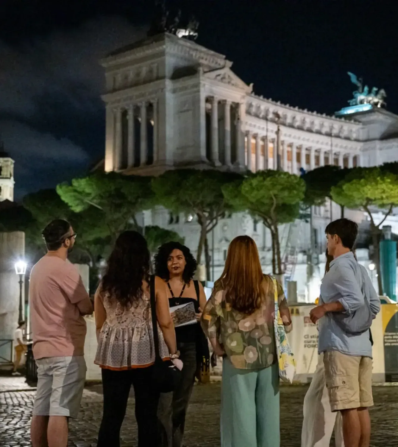 Tour group gathered in front of the illuminated Altar of the Fatherland with classical architecture at night