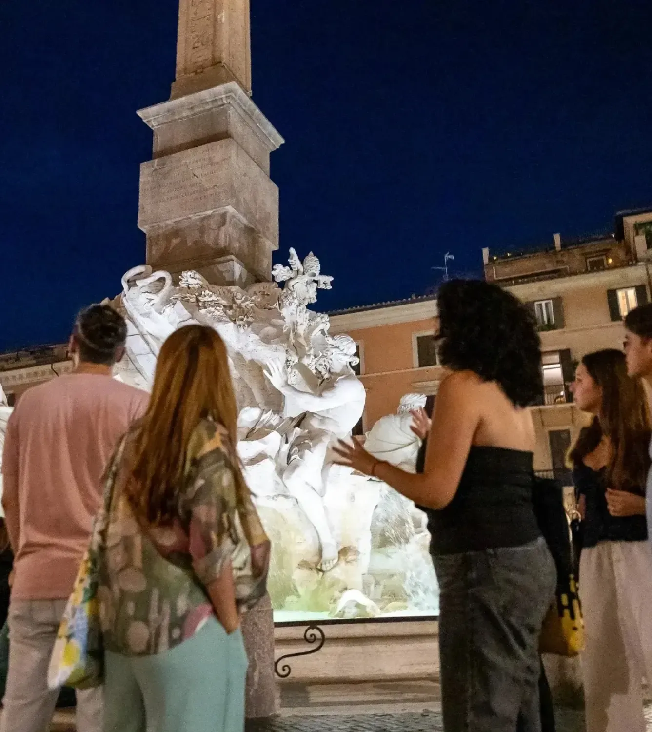 Tour group gathered around the illuminated Fountain of the Four Rivers at Piazza Navona at night